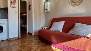 Una habitación compacta con sofá rojo, lavadora y pequeña zona de cocina.