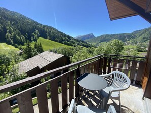 En balkon med bord og stole, udsigt over et bjerglandskab med grønne dale og spredte bygninger.