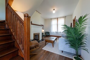A spacious living room with a wooden staircase, a fireplace, a sofa, and a large green plant. - Historic Swiss Chalet Overlooking the Rockies (Golden)