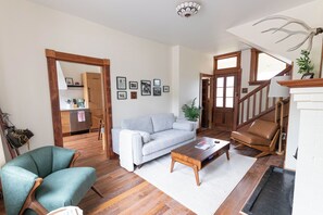 A living room with a sofa, armchair, coffee table, and a staircase with a lamp. - Historic Swiss Chalet Overlooking the Rockies (Golden)