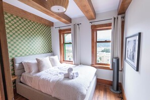 A bedroom with a bed, a window, a wall-mounted TV, and a view of the city. - Historic Swiss Chalet Overlooking the Rockies (Golden)