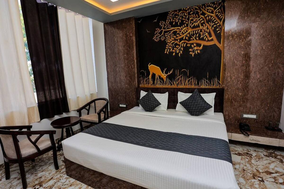 A hotel room with a large bed, a desk, and chairs. There is a wall art of a tree and deer.