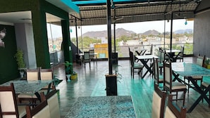 An outdoor restaurant with multiple tables and chairs, surrounded by potted plants and a view of the cityscape and mountains. - Hotel Eagle Inn (Udaipur)