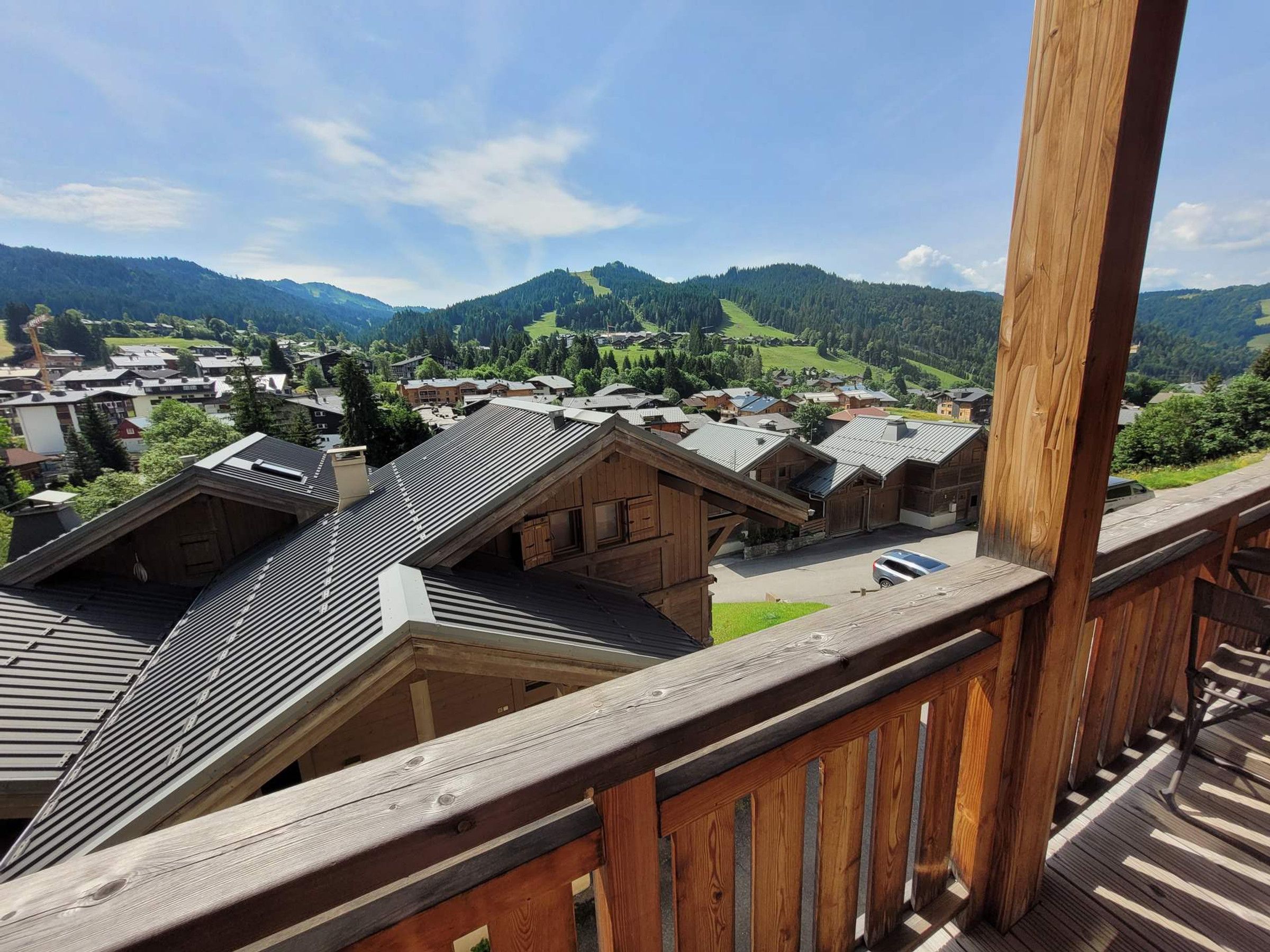 A wooden balcony overlooking a village with traditional houses and a mountainous backdrop.