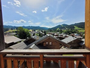 Un balcón de madera con vistas a un pueblo con casas tradicionales y montañas al fondo.