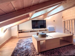 Een moderne zolderkamer met een grote televisie, houten meubels en een gezellig vloerkleed.
