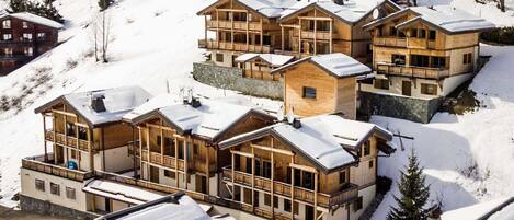 Un grupo de chalés de madera con balcones, ubicados en una ladera nevada.