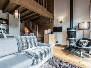 A modern living room with a grey sofa, a fur throw, a black chair, a fireplace, and a staircase leading to an upper level. - Cozy apartment 2 en-suite bedrooms, close to shops, covered parking (Les Gets)
