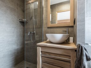 A modern bathroom with a glass-enclosed shower, a wooden vanity with a white vessel sink, and a mirror above the sink.