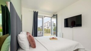 A modern hotel room with a large bed, a flat-screen TV mounted on the wall, and a sliding glass door leading to an outdoor balcony. - Stylish Apartment in Lukecin | Pool, Terrace, Parking (Lukecin)