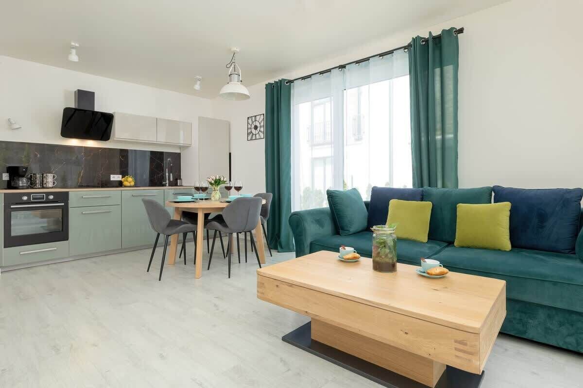 A modern living space with a kitchen, dining area, and a green sofa with cushions.