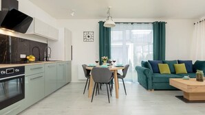 A modern kitchen with a built-in oven, a dining table with chairs, and a teal sofa with cushions. - Stylish Apartment in Lukecin | Pool, Terrace, Parking (Lukecin)