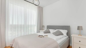Ein modernes Schlafzimmer mit einem Bett, Nachttischen und einem Fenster mit transparenten Vorhängen.