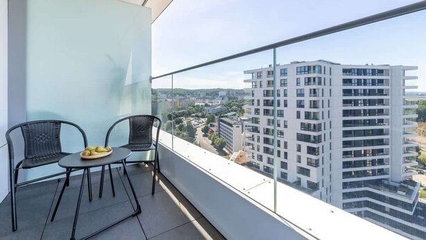 Ein Balkon mit zwei Stühlen und einem kleinen Tisch, mit Blick auf ein modernes Gebäude.