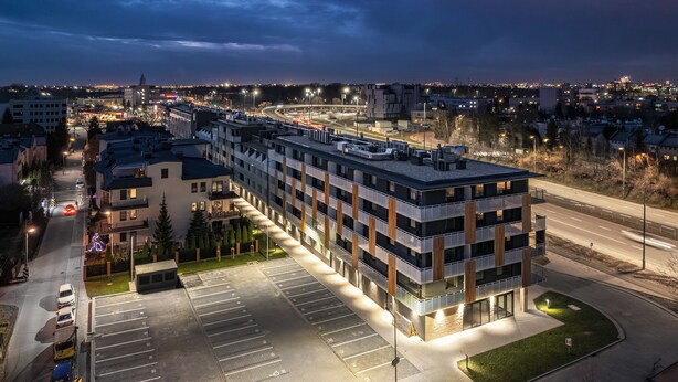 A multi-story parking garage with a modern design, adjacent to a road with visible traffic. - RentPlanet - Apartament Pileckiego (Warsaw)