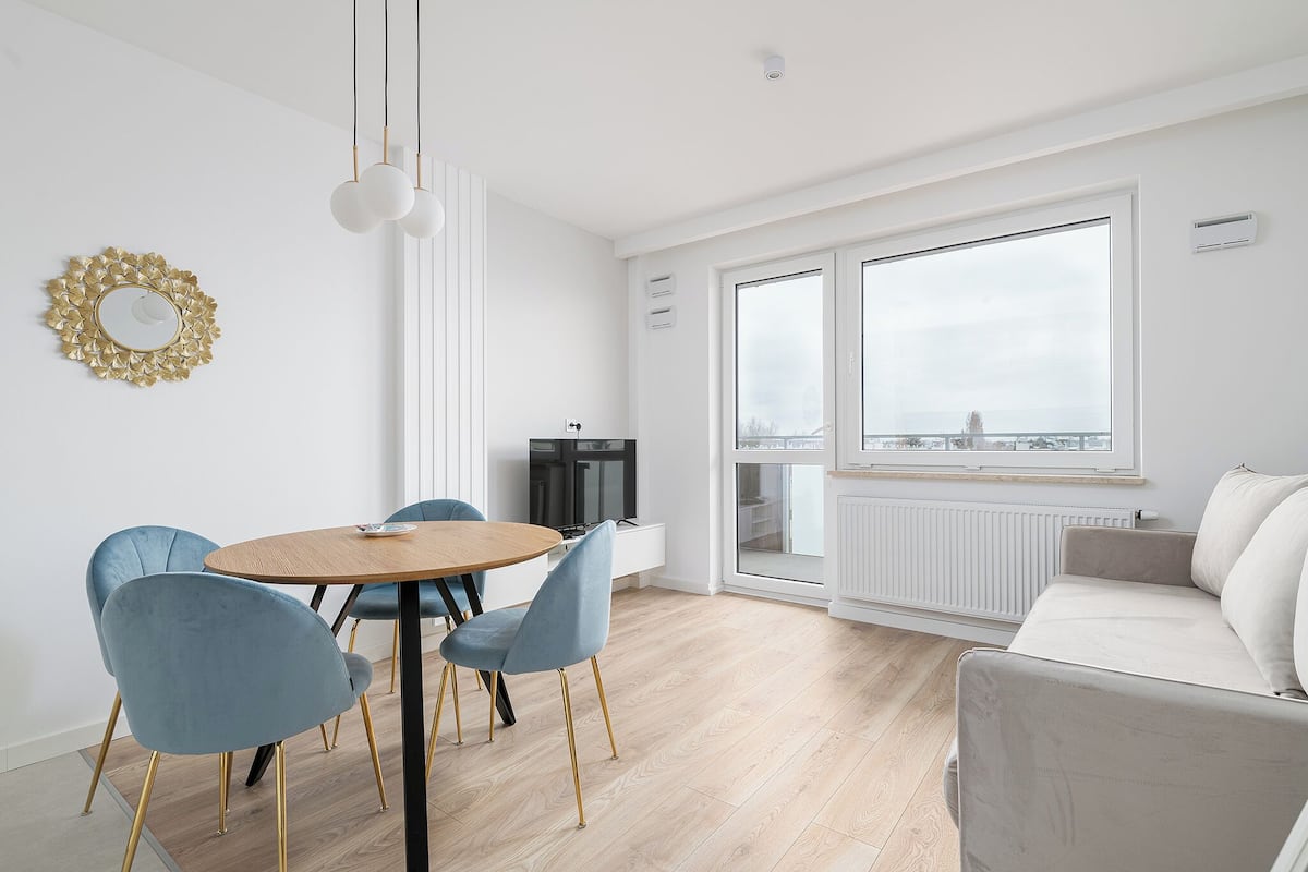Ein modernes Wohnzimmer mit einer Couch, einem Esstisch mit Stühlen, einem Fernseher und einem großen Fenster mit Ausblick.