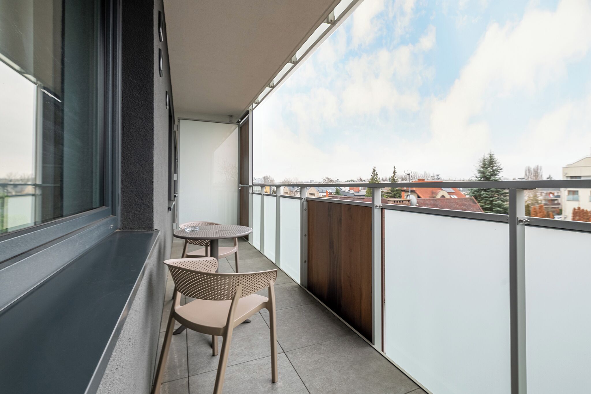 A balcony with two chairs and a small table, overlooking a residential area.