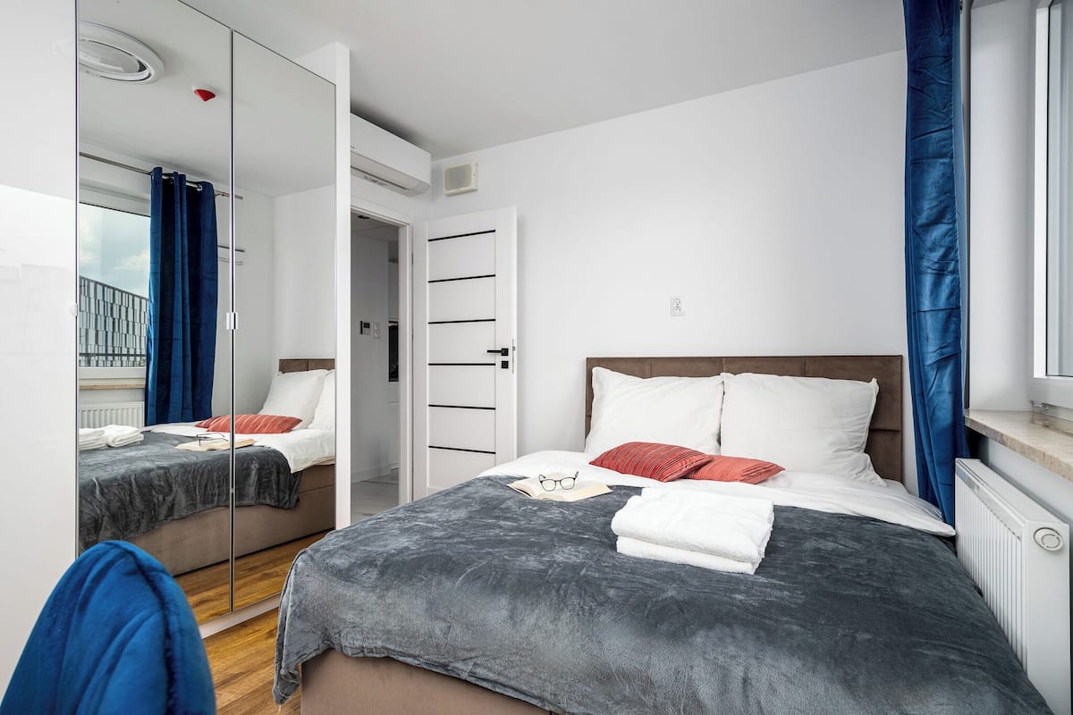Ein modernes Hotelzimmer mit einem großen Bett, einem Spiegel, einem Kleiderschrank und einem Fenster mit Vorhängen.