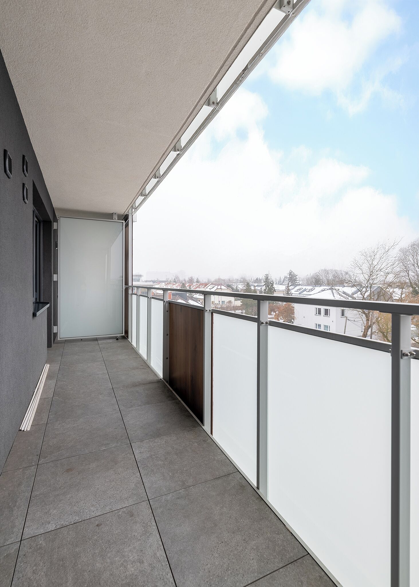 Een balkon met uitzicht op een woonwijk, een metalen hekwerk en een betegelde vloer.