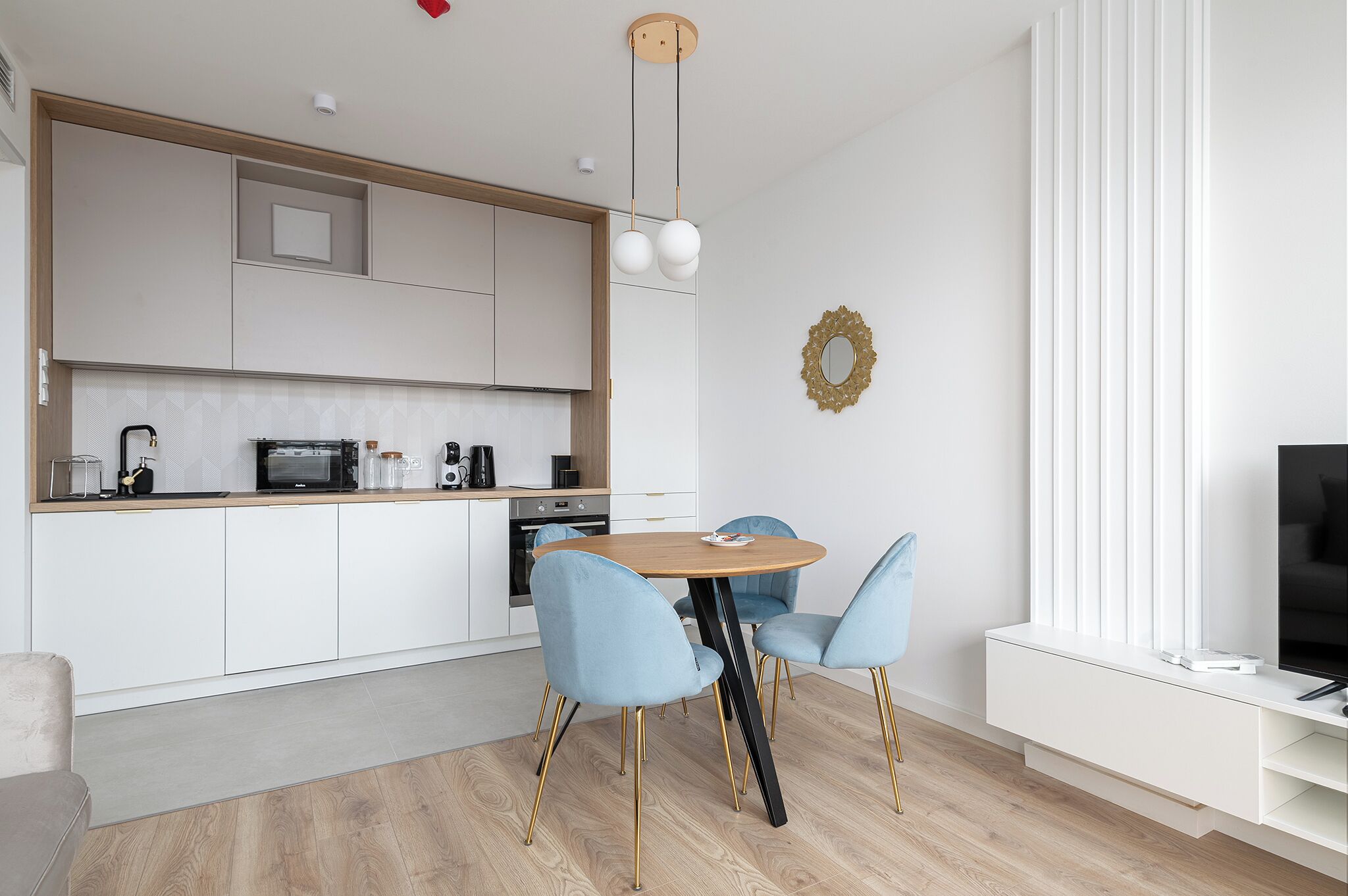 A modern kitchen with white cabinets, a wooden dining table, and two blue chairs.
