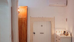 Une pièce avec une porte en bois, une commode blanche à tiroirs, une petite table avec une théière et un tapis à motifs sur le sol.