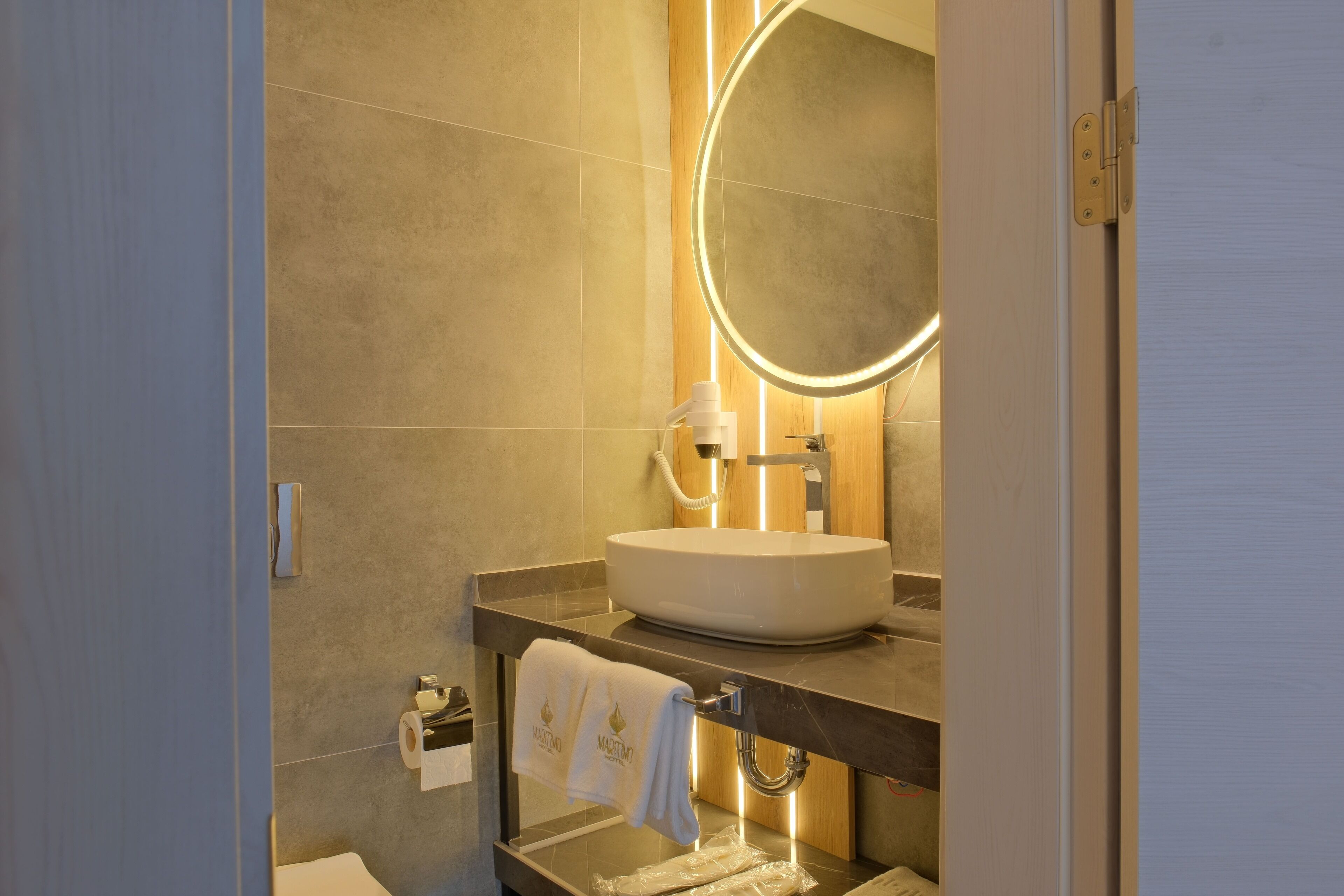 Un baño moderno con un espejo redondo, un lavabo blanco y un perchero para toallas.