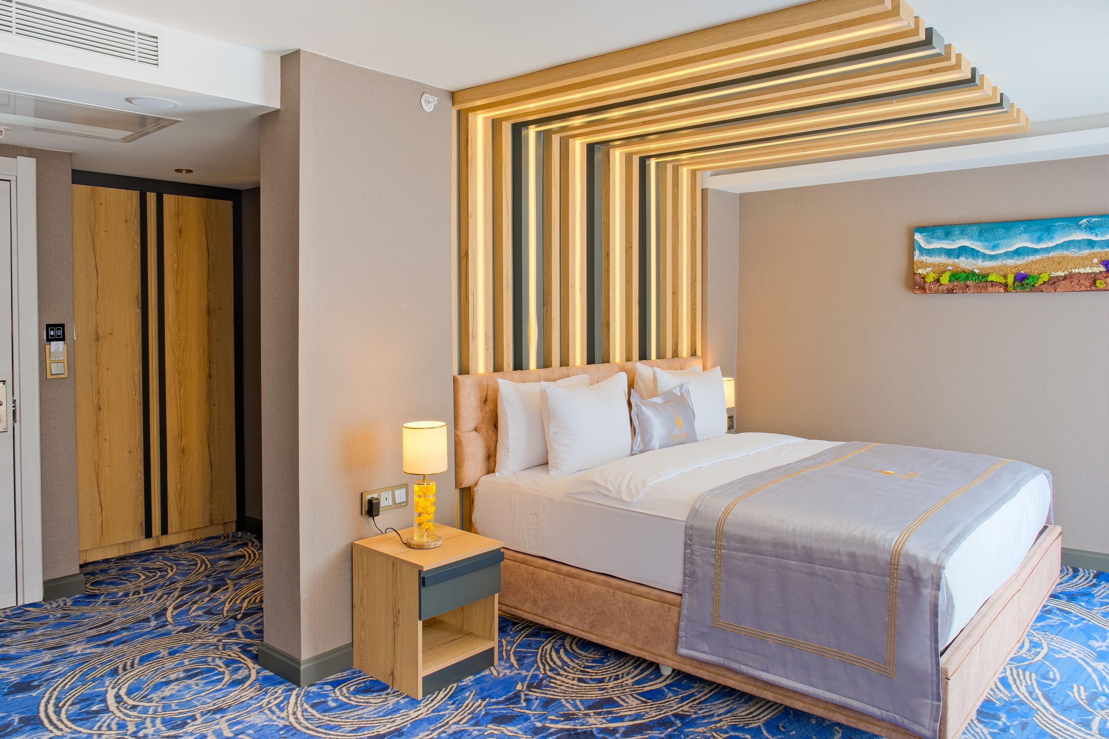 A hotel room with a bed, a nightstand, a painting, and a patterned carpet.