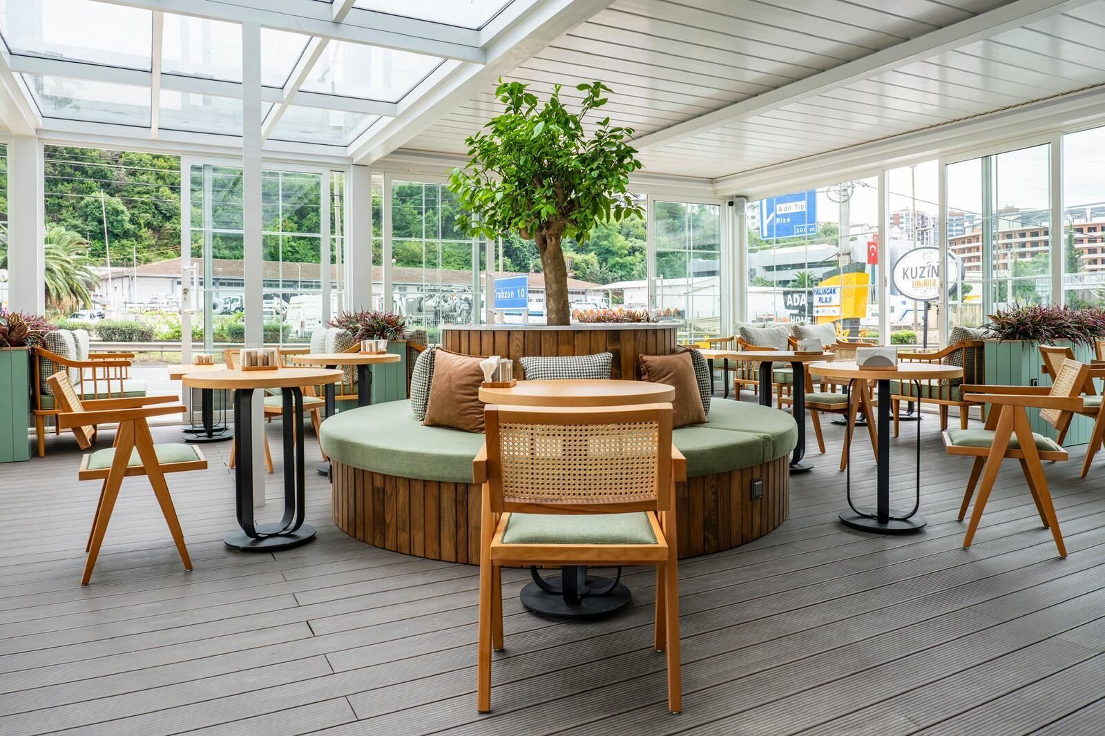 An indoor seating area with round tables and chairs, a central cushioned seating area, and a large tree.