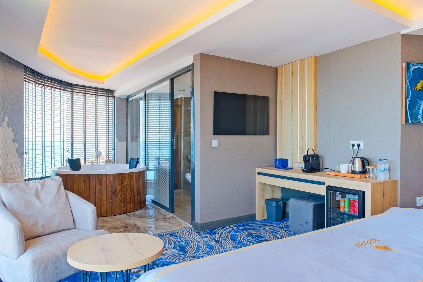 Habitación de hotel con cama, sofá, una mesita redonda, tocador de madera con lavamanos, televisor de pantalla plana y minibar.