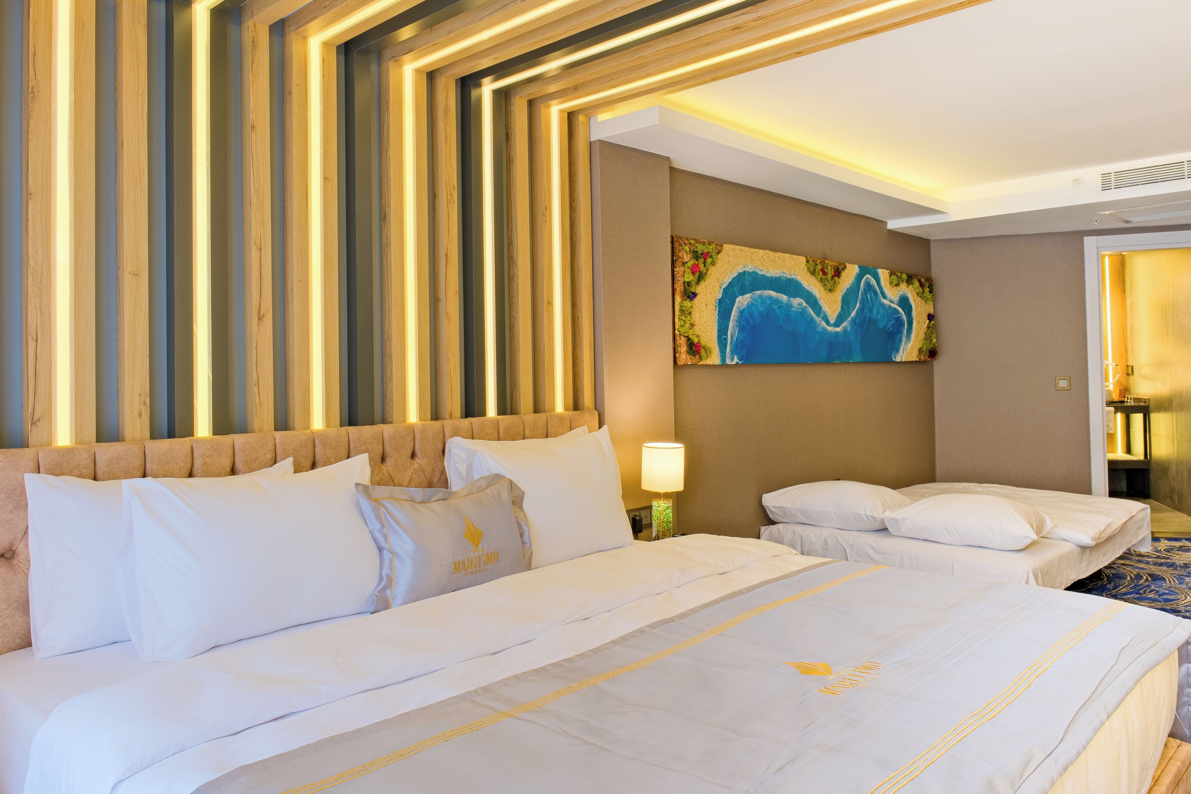 A hotel room with a large bed, a headboard, a painting on the wall, and a lamp.