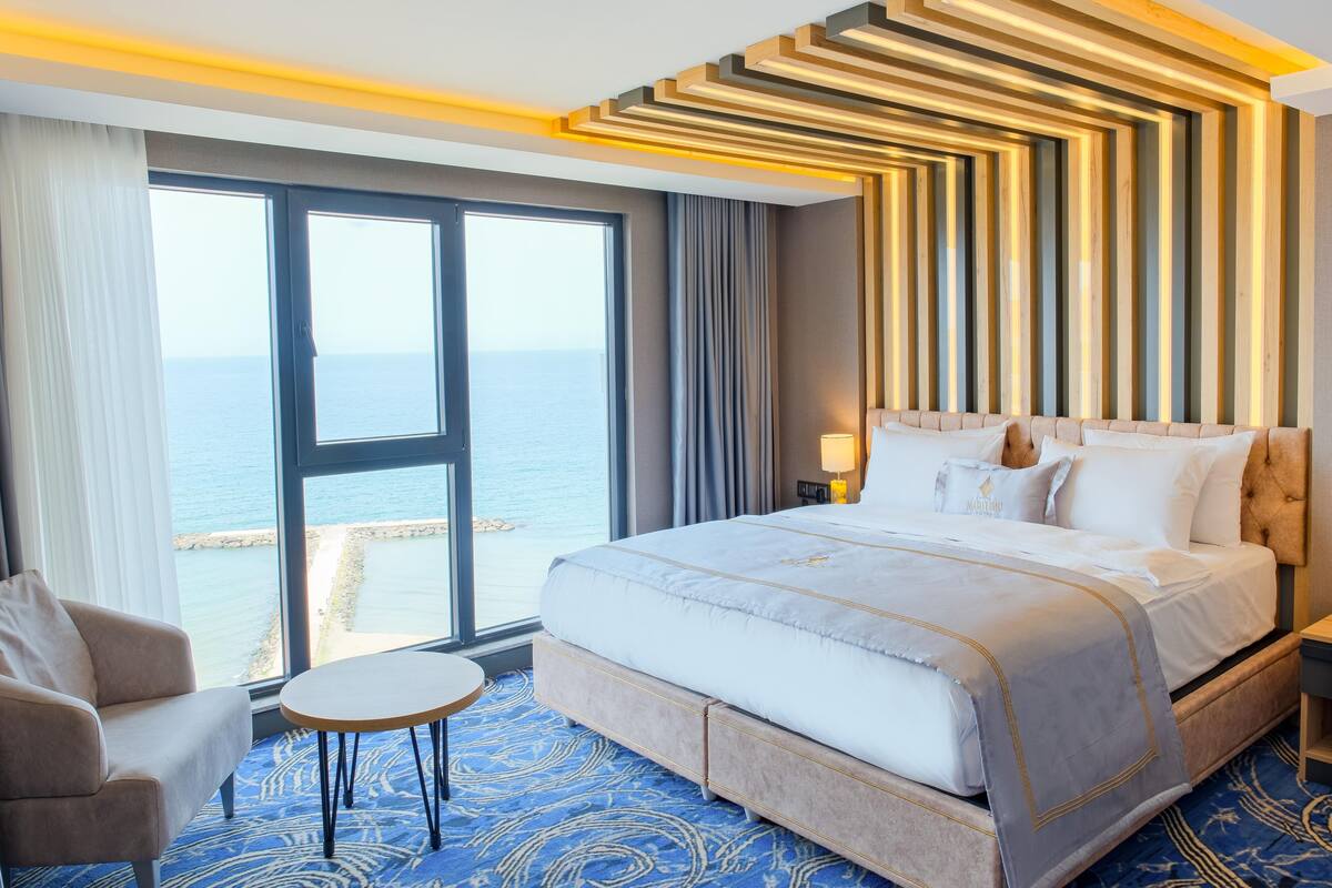 Quarto de hotel com uma cama grande, um sofá, uma mesinha e vista para o mar.