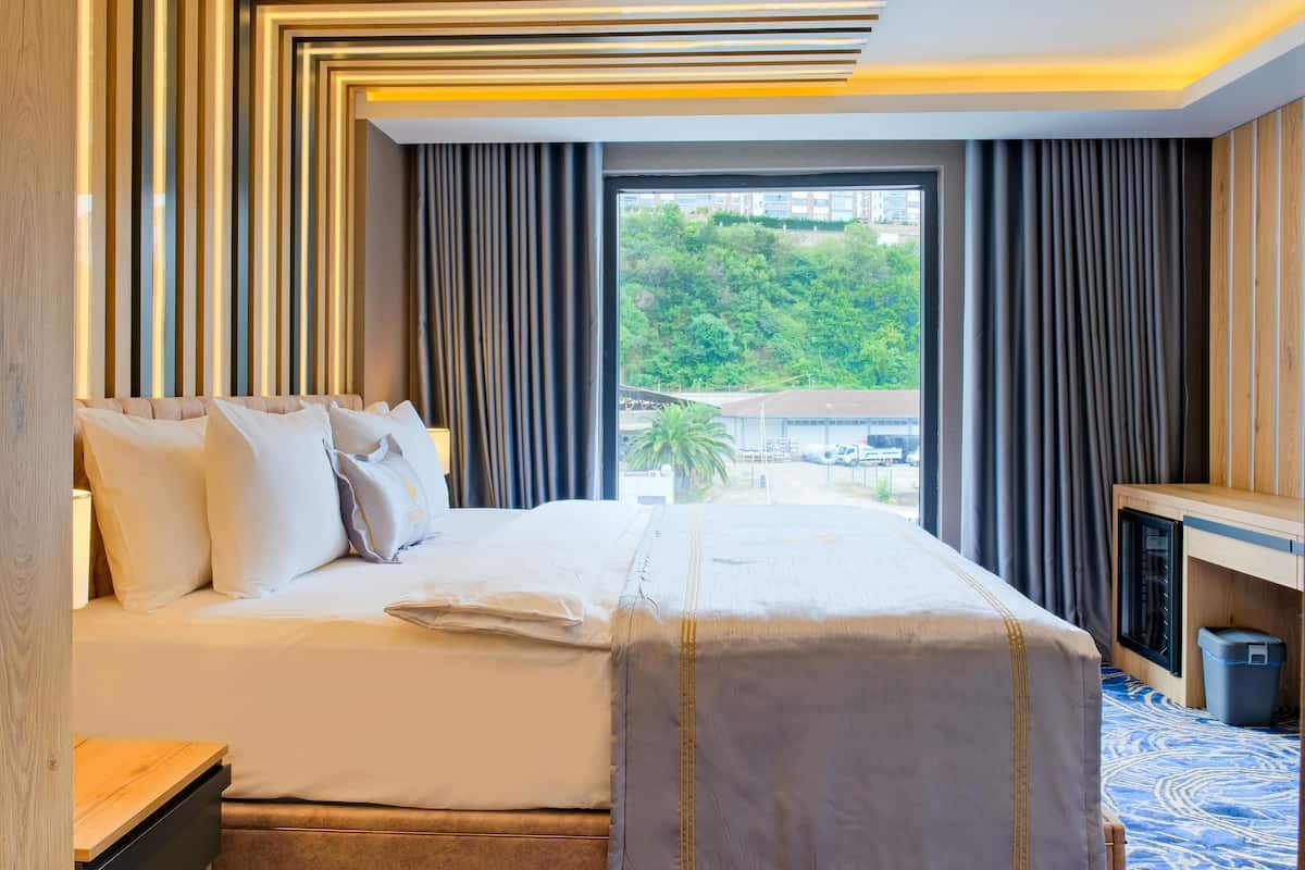Quarto de hotel com uma cama grande, vista para o verde lá fora e design moderno com painéis de madeira e um tapete estampado.