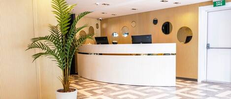 A reception area with a curved reception desk, a potted plant, and a patterned floor.