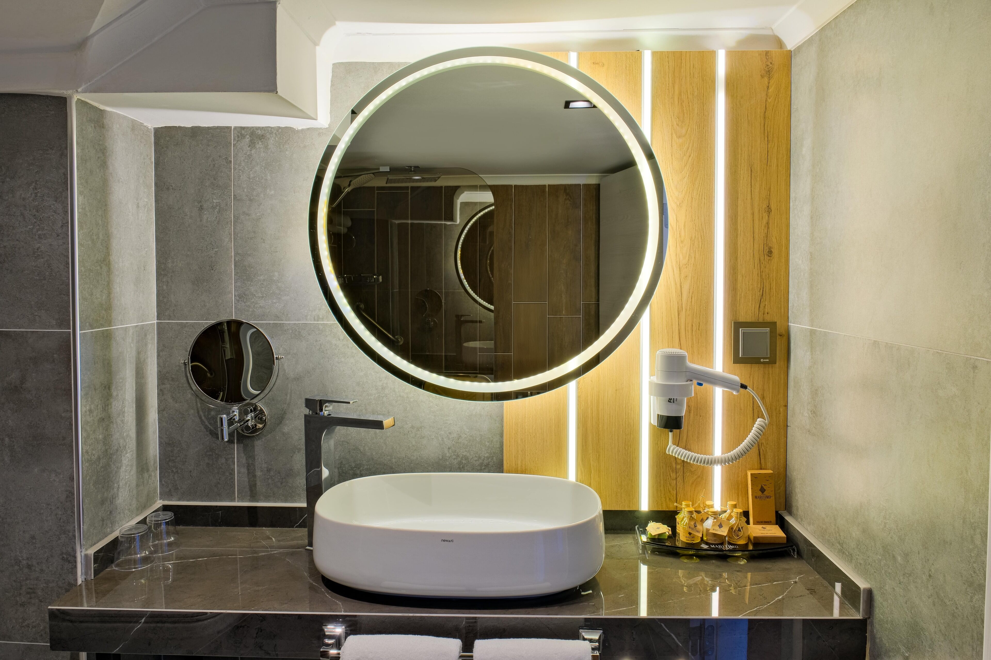 A modern bathroom with a round mirror, a white sink, and a handheld hairdryer.