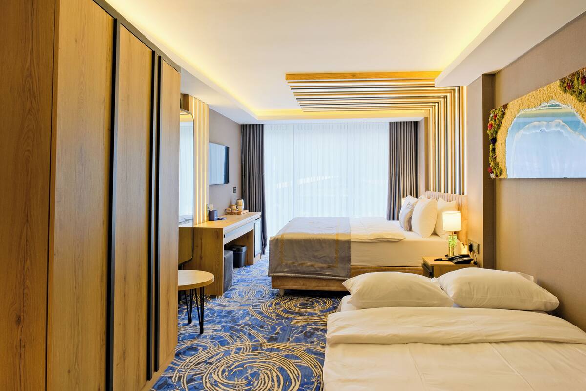 Quarto de hotel com uma cama grande, uma mesa, uma cadeira e uma janela com cortinas.