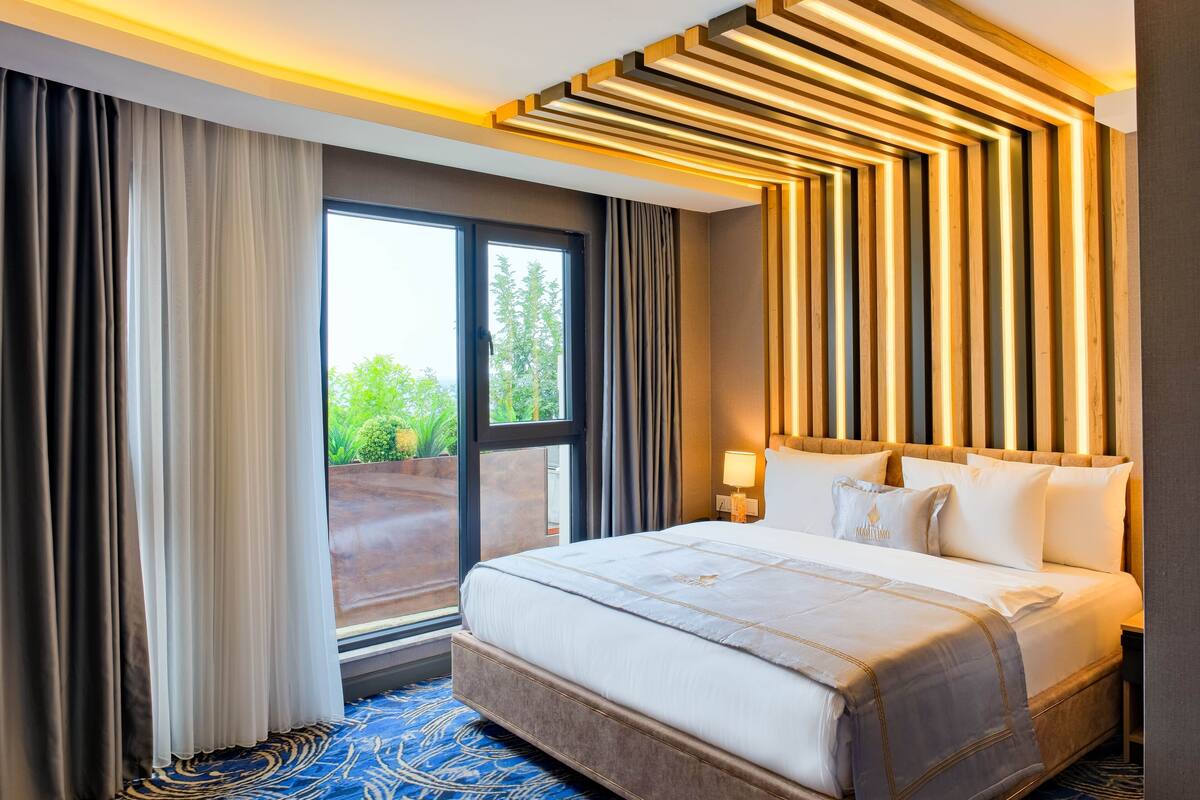 Quarto de hotel com uma cama grande, vista para o verde lá fora e um design moderno no teto.