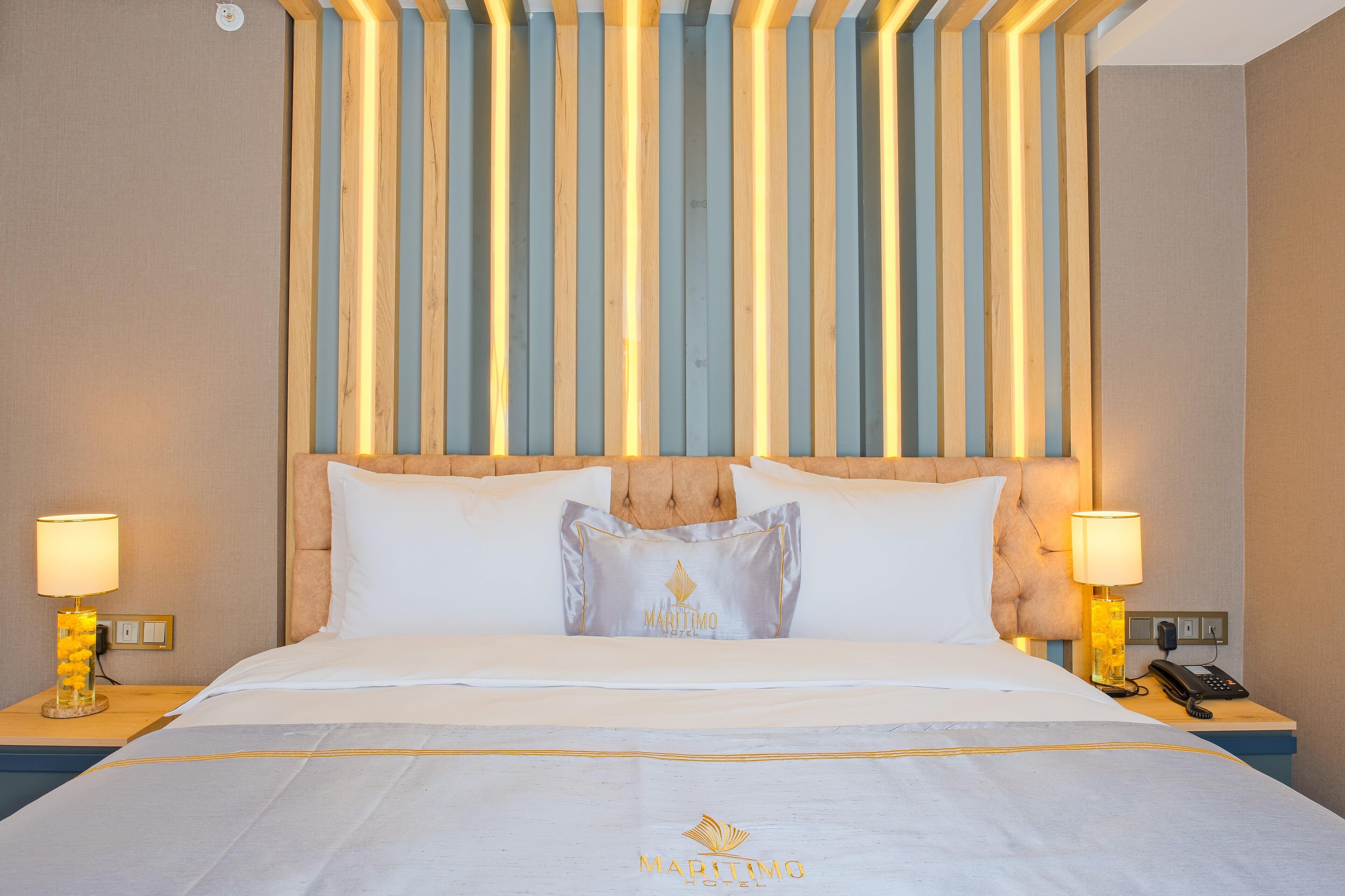 Een hotelkamer met een bed, twee nachtkastjes, een lamp en een wand met verticale houten lamellen.