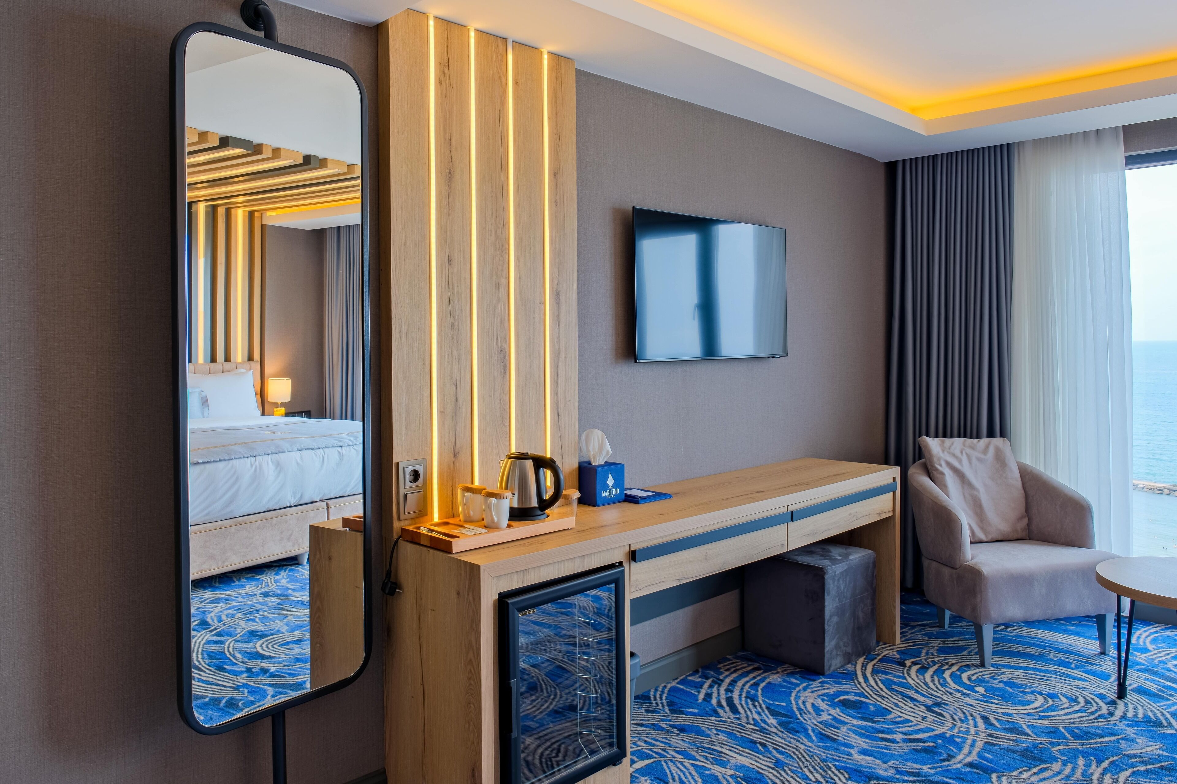 A hotel room with a bed, a desk, a chair, a TV, and a large window.
