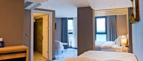 Habitación de hotel con cama, mesita de noche y escritorio. Se ve un baño por una puerta abierta.