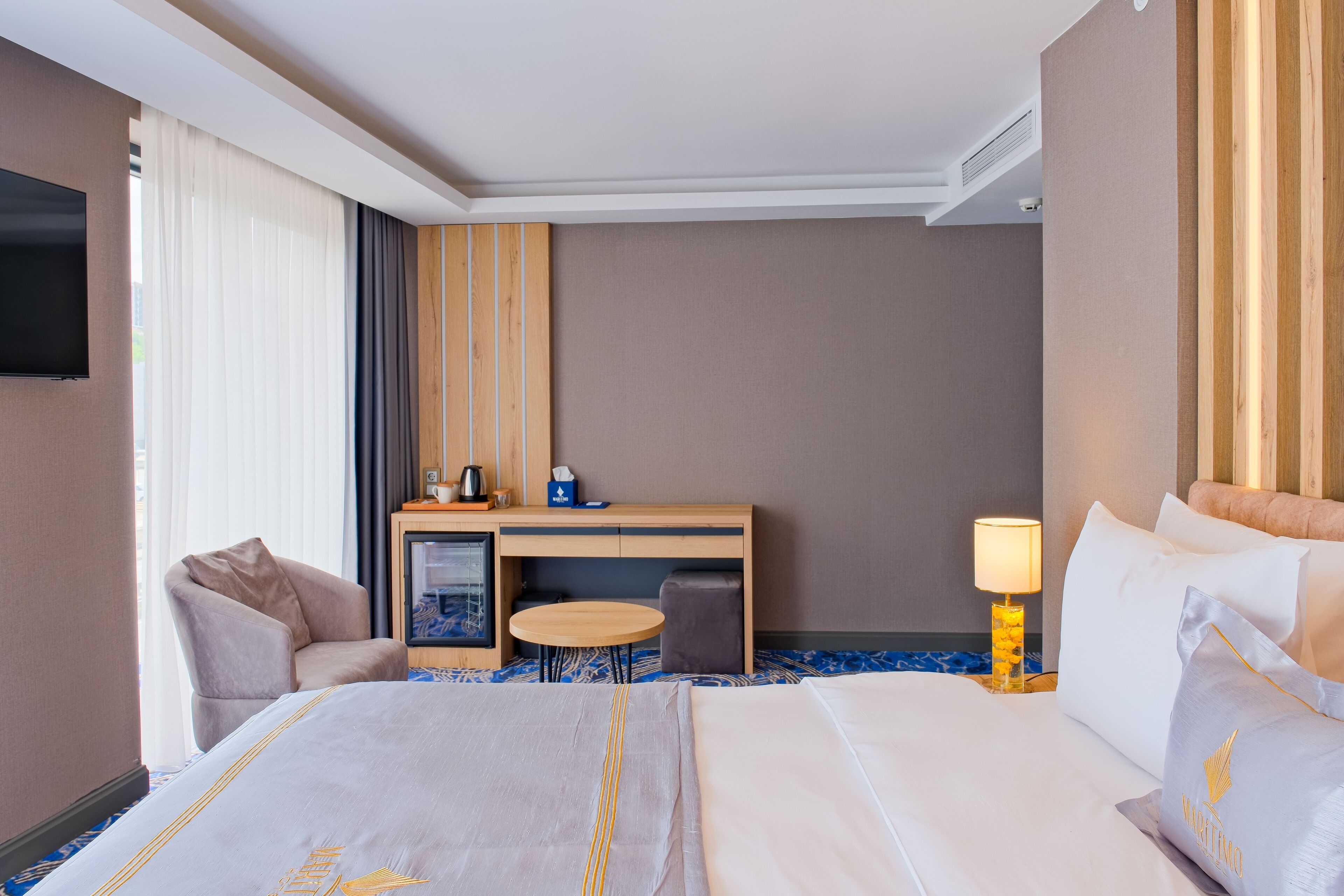 Habitación de hotel con cama, escritorio, silla, una mesita, lámpara y televisor.