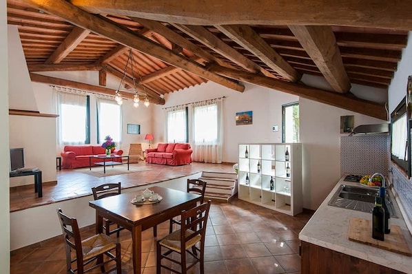 A spacious living area with a dining table, red sofas, and a kitchen with a tiled backsplash.