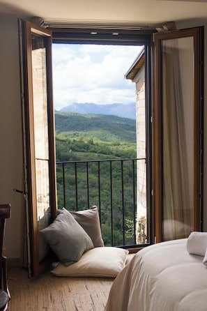Quarto com vista para uma paisagem montanhosa através de uma porta de varanda aberta.