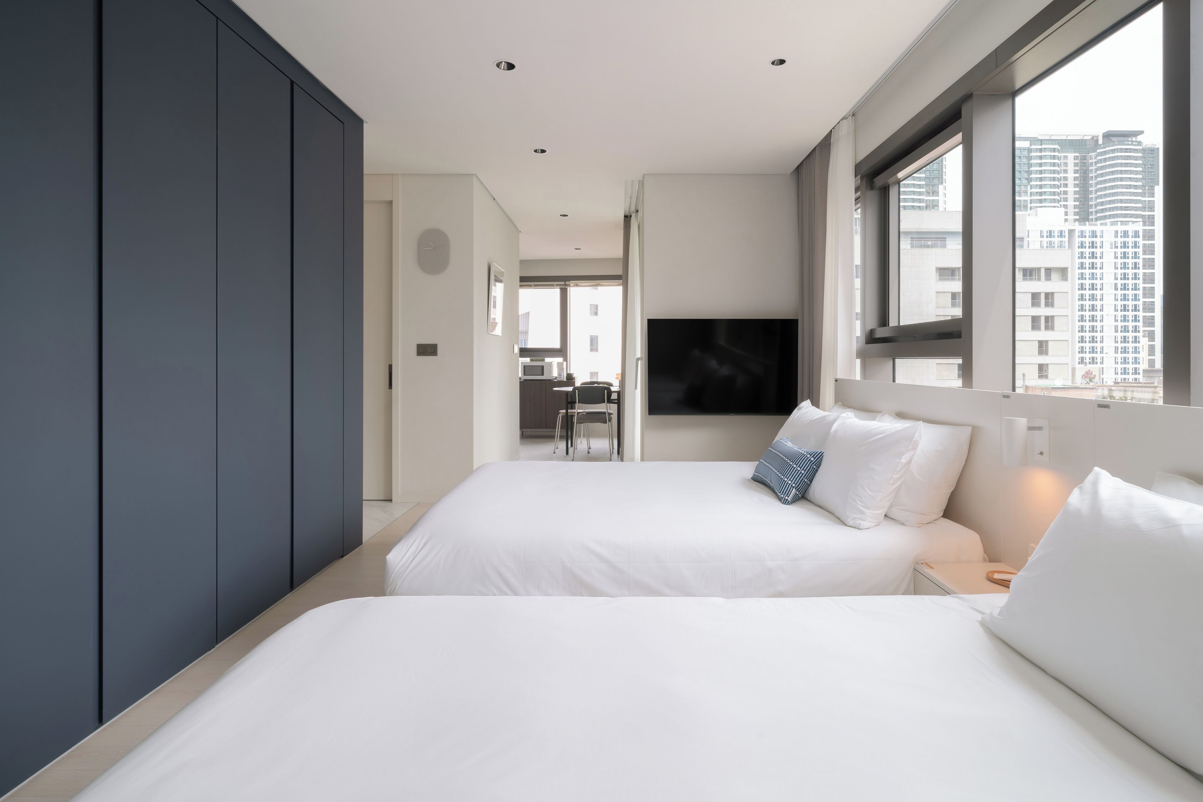 A modern hotel room with two beds, a TV, and a city view.