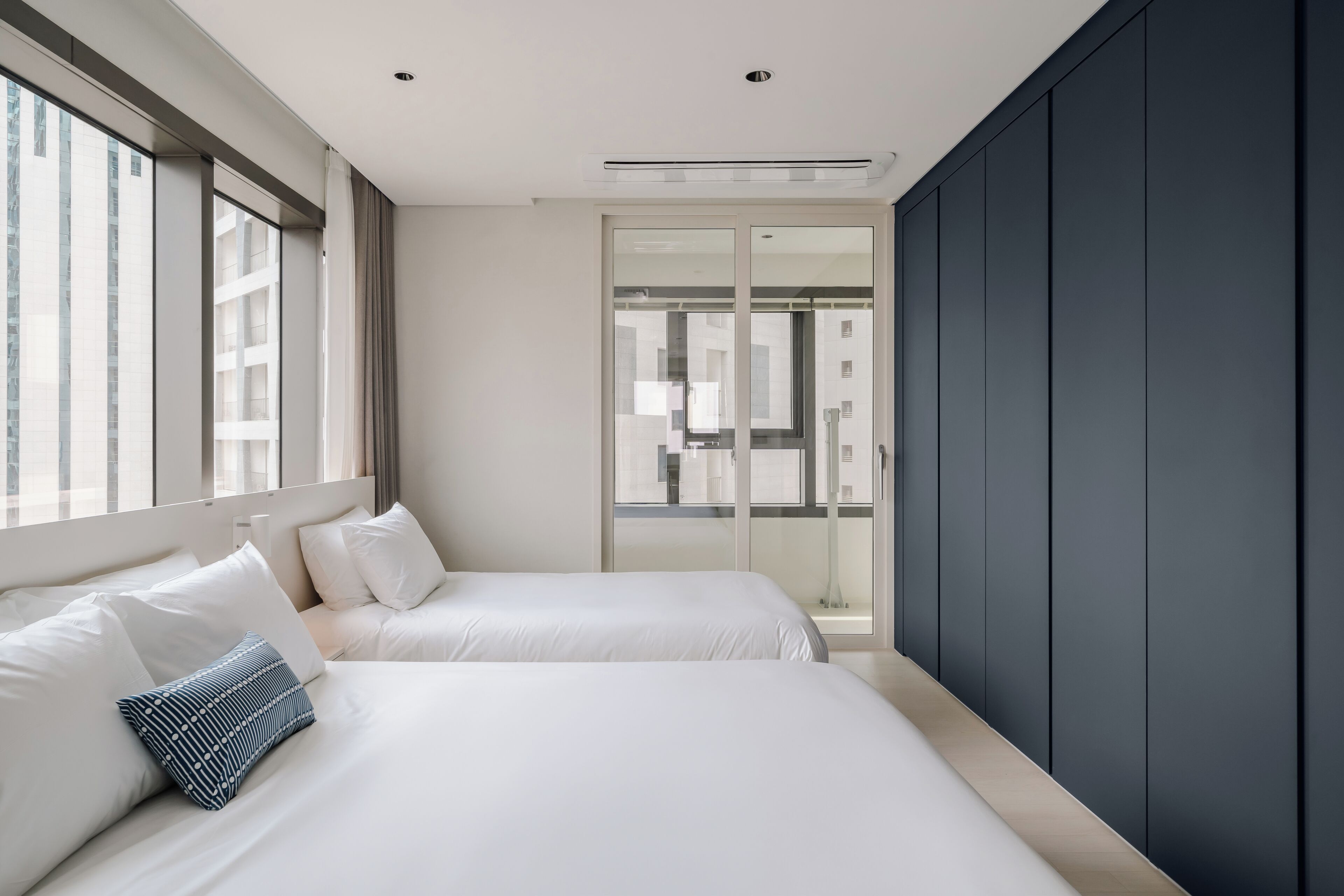 Una habitación de hotel moderna con dos camas, un ventanal grande y vistas a la ciudad.