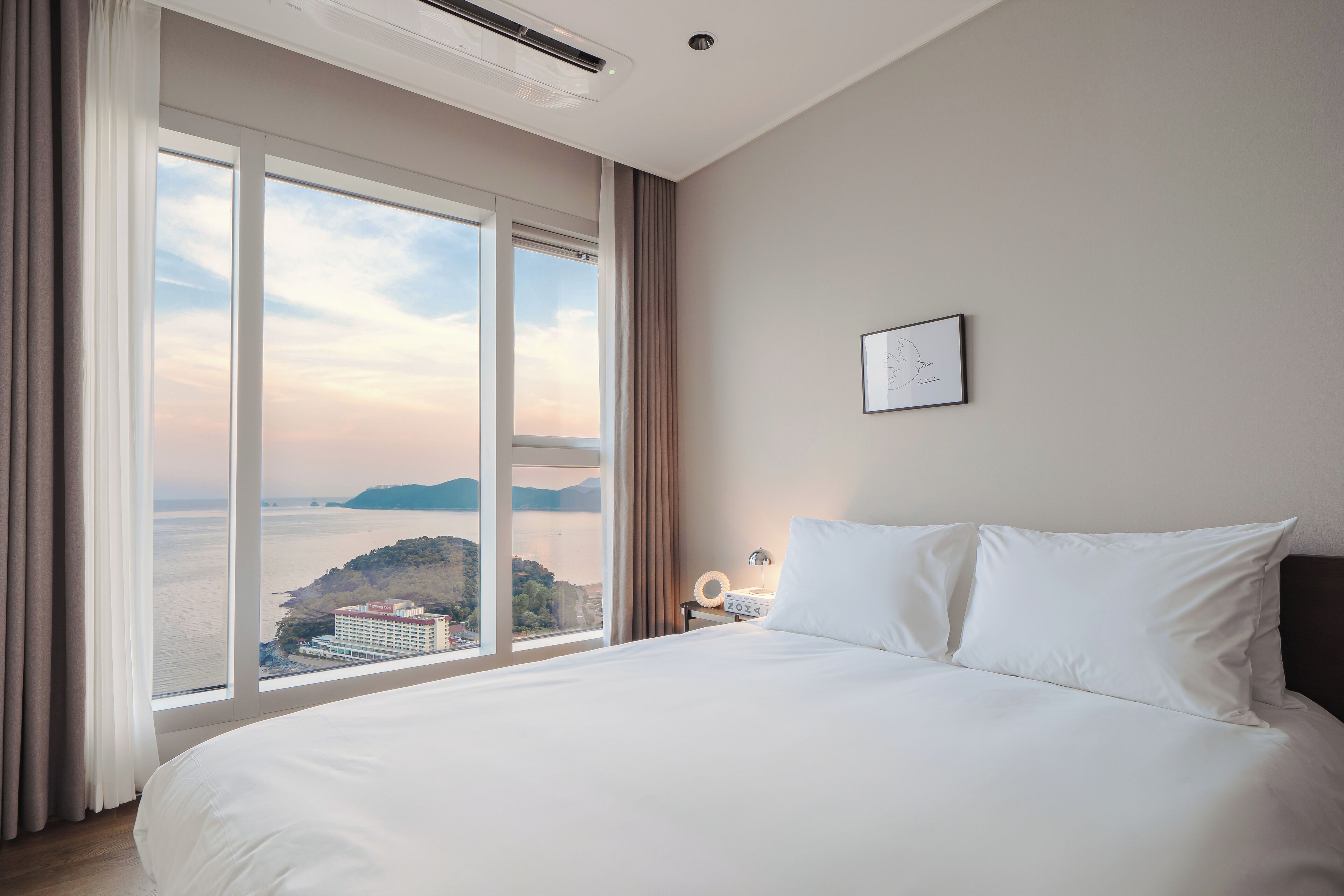 A hotel room with a large bed, a nightstand, a lamp, and a framed picture on the wall.