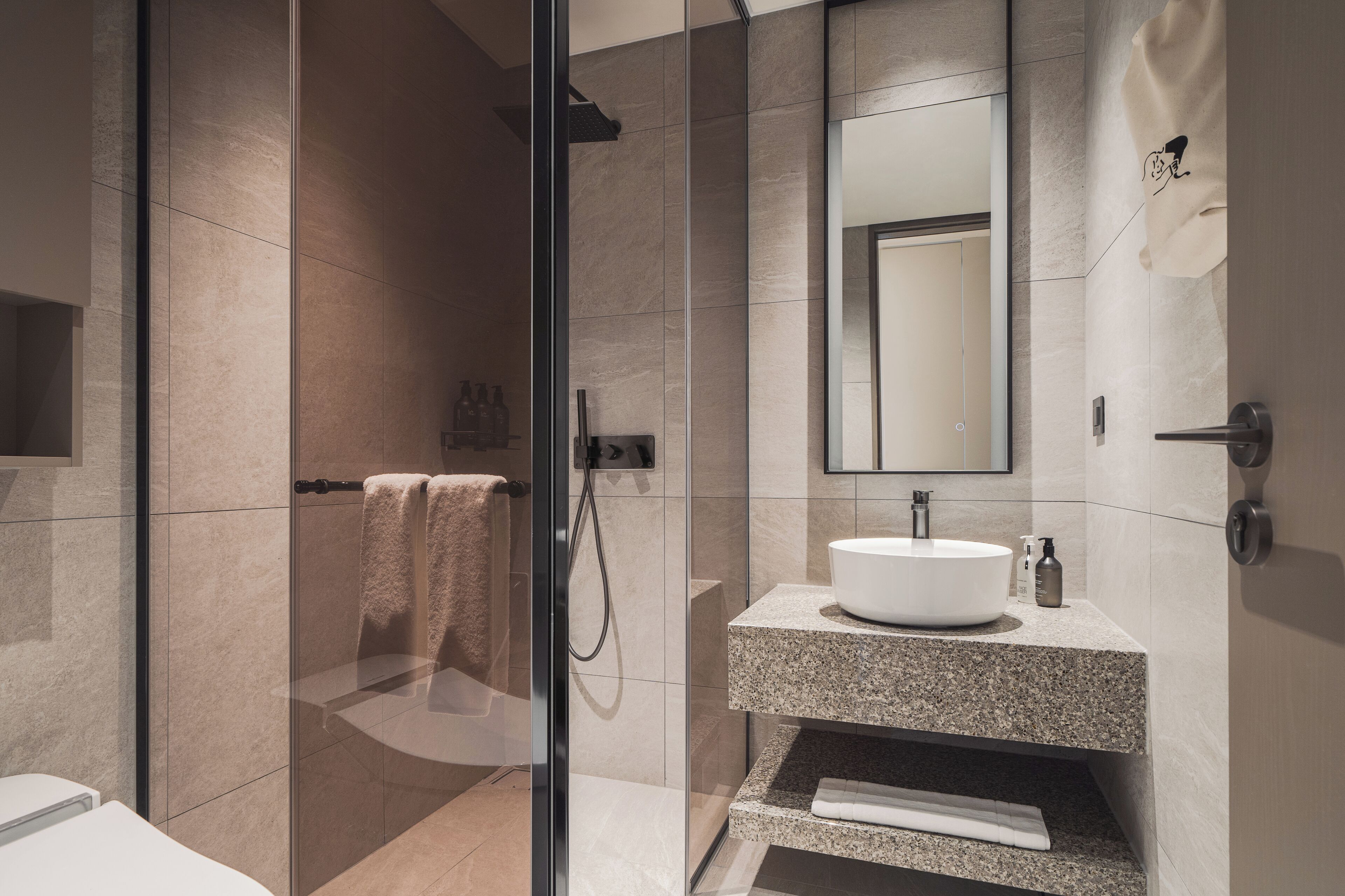 A modern bathroom with a glass-enclosed shower, a granite countertop sink, and a large mirror.