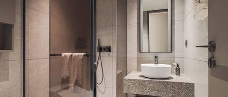 A modern bathroom with a glass-enclosed shower, a granite countertop sink, and a large mirror.