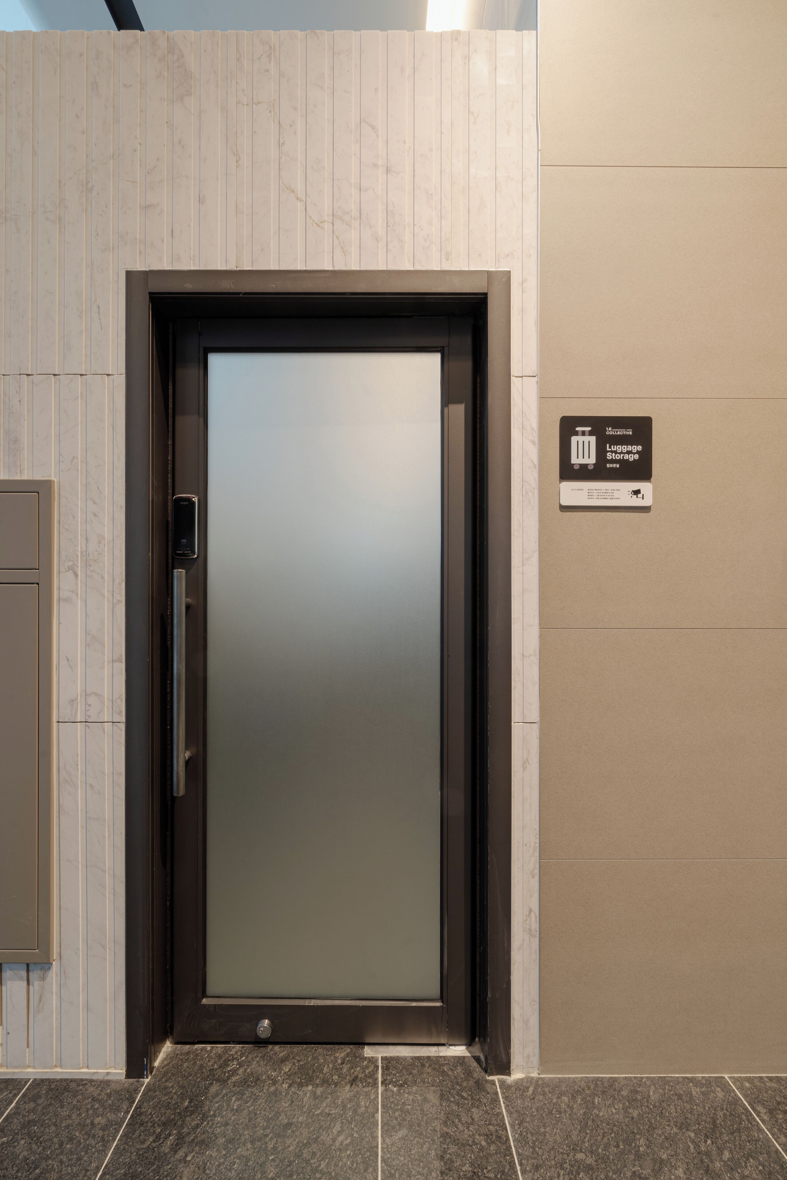Un moderno ascensor con puerta de vidrio satinado, un letrero de almacenamiento de equipaje y un agarrador metálico.