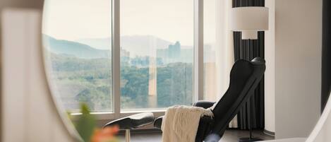 Una habitación moderna con un ventanal grande, un sillón reclinable negro, una manta blanca y una lámpara de pie.