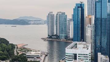 A high-rise building with a curved glass facade, adjacent to a waterfront with a bridge and a parking lot.